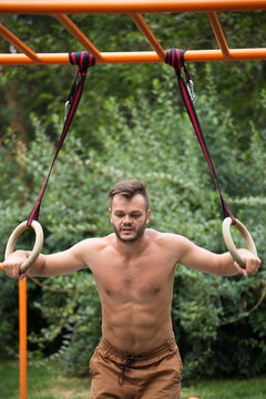 Muscular man exercising on outdoor gymnastic ring.