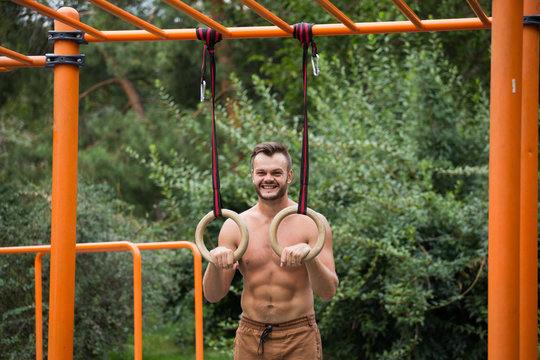 Muscular man exercising on outdoor gymnastic ring.
