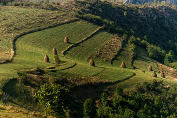 Amazing Romanian countryside in mountains with haystacks on pasture in the summer afternoon light