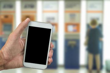 Man use mobile phone, blur image of people use ATM machine as background.