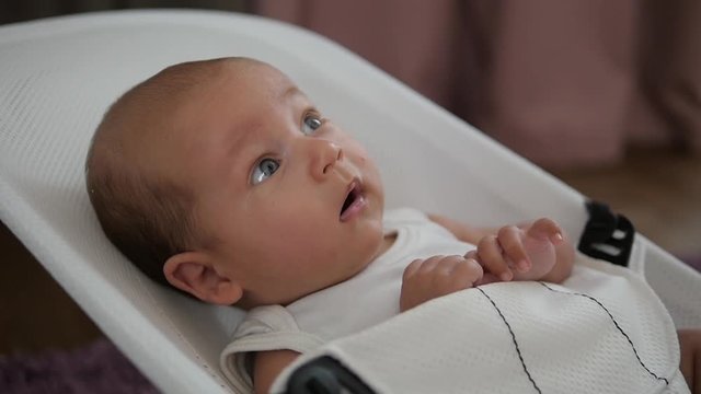 Amazed baby boy with wide-open eyes being rocked in a chair. handheld shot