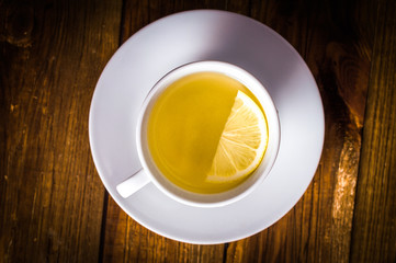 White cup of tea with half a lemon. On a wooden background.