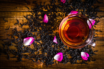 A cup of black tea. Tea leaves with rose petals. On a wooden background.