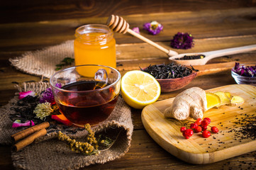 A cup of black tea on sackcloth. Cinnamon, Honey, loose tea, ginger, flowers, board, petals. On a...