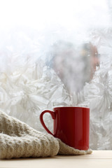 warming power of love/ red mug of hot drink with melted frosty window in the form of a heart symbol 