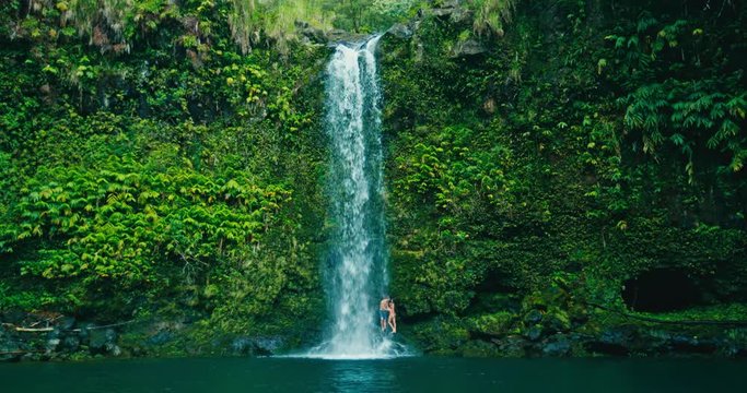 Attractive adventurous young couple relaxing under beautiful waterfall