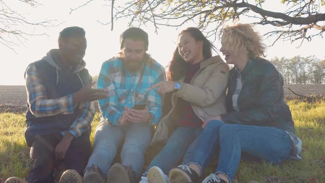 Diverse quartet of friends taking a self portrait with their camera phone while laying down on grass outside