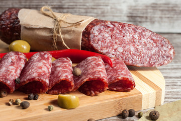 Italian salami with olives and spices on wooden background