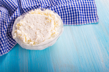 Cottage cheese in a bowl with a napkin. On blue, wooden background.