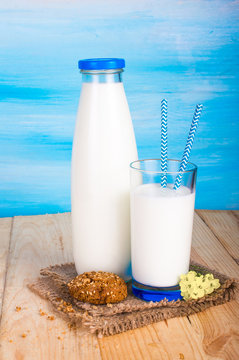 A bottle of milk, a glass of milk with straws and cookies. On a blue background.