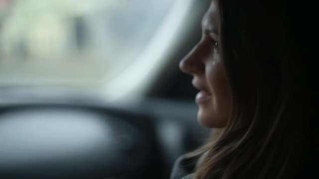 Side view of a pretty young woman talking. Brunette girl sitting in a car on the go.