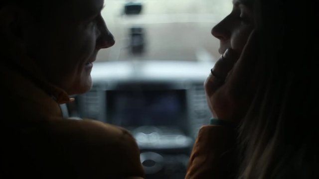 Loving couple sit in car and have a conversation. Man and woman laugh, talk, kiss, he gently touches her face.