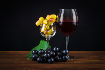A glass of wine, grapes and leaves. On a wooden background.
