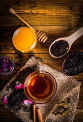 A cup of black tea on sackcloth. Cinnamon, Honey, loose tea, petals. On a wooden background.