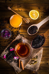 A cup of black tea on sackcloth. Cinnamon, Honey, loose tea, petals. On a wooden background.