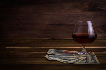 Glass of whiskey with money on a wooden table.