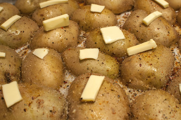 Tray with baked potatoes in oven with butter and spices closeup as food background