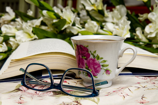 Concept image with open book, coffee cup, reading glasses with flowers in background.