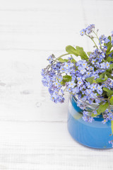 small blue flowers in a jar on a white wooden background