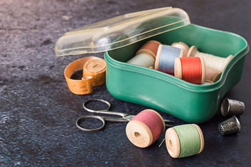   Sewing supplies. A box with wooden spools of thread, old scissors and two thimbles on a blue background.