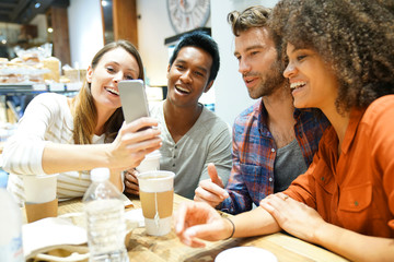 Group of friends in coffee shop looking at smartphone