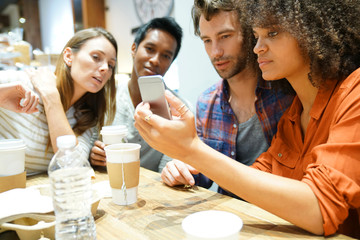 Group of friends in coffee shop looking at smartphone