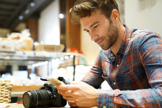 Man in coffee shop checking pictures with camera and smartphone