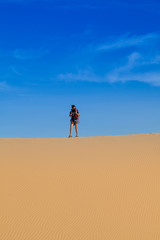 Female photographer with her backpack travelling in windy white sand dunes at Muine desert, Phan thiet, Vietnam
