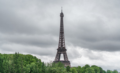 Fototapeta premium The Eiffel Tower over trees, stormy clouds