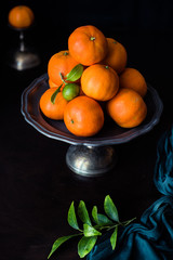 mandarino verde acerbo con foglie in un piatto per dolci in metallo vicino a altri mandaranci....