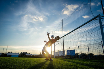 Fototapeta na wymiar Football player is training at the field on a sunset background