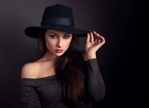 Elegant makeup woman in fashion hat posing on dark shadow backgr