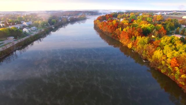 Sunrise over steaming autumn river, Fall colors adorning shore, aerial view.

