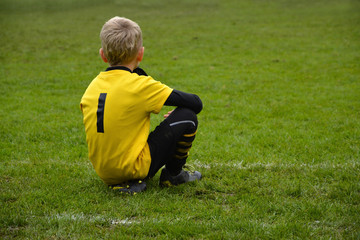 Fototapeta na wymiar A young boy dressed in a jersey with the number one sitting on the grass