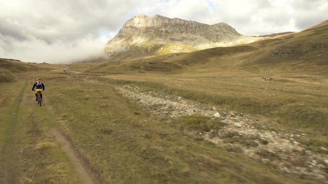 Aerial shot of mountain biker riding a grass covered trail on alpine pass in autumn season
