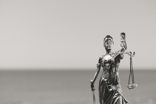 Justice Themis goddess sculpture on bright sky copy space background. Black and white image