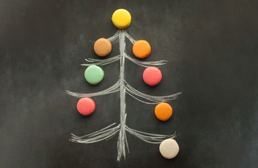 Christmas tree, drawn with a piece of chalk on the chalkboard, decorated with colorful macaroons from different tastes.