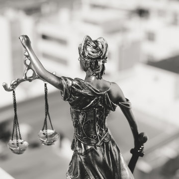 Back view of Lady Justice, statuette of the Themis goddess. Law concept. City buildings outdoor background