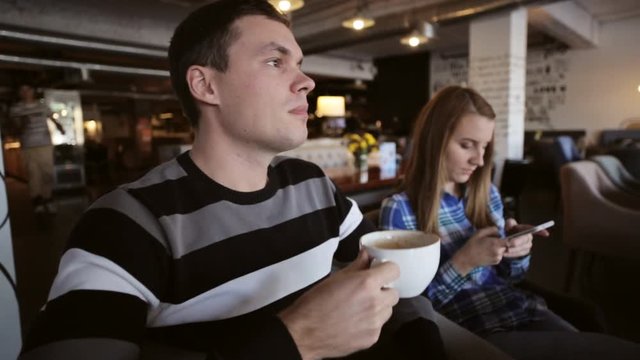 Young couple in cafe. Male drinking coffe while female using smartphone