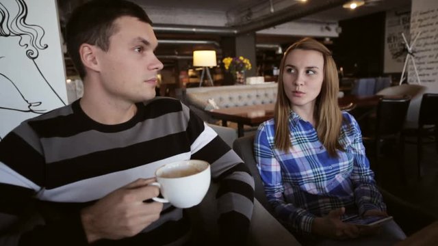 Young couple in cafe. Male drinking coffe while female using smartphone