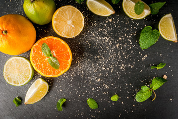 Fresh citrus fruits on a black slate table - tangerine, lime, lemon, mint leaves and brown cane sugar. Top view