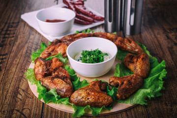delicious grilled chicken wings with garlic and tomato sauce with lettuce on a round board on wooden rustic background