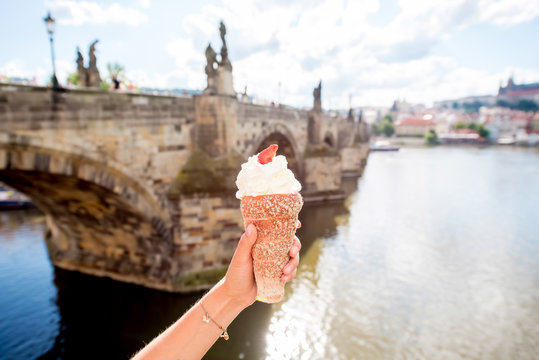 Female hand holding traditional czech cookie called trdelnik on the river background in Prague.