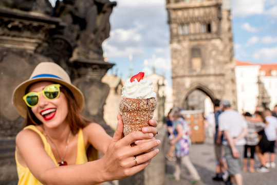 Young female tourist with traditional czech dessert called trdelnik on Charles bridge in Prague