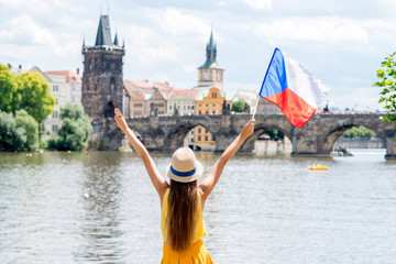 Fototapeta Young female tourist with raised hands holding czech flag on the old town background in Prague. obraz