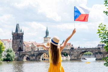 Young female tourist with raised hands holding czech flag on the old town background in Prague.
