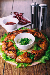 delicious grilled chicken wings with garlic and tomato sauce with lettuce on a round board on wooden rustic background