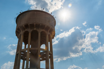 Looking up to a large cement reservoir with clouds behind the water tower