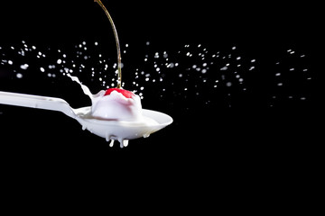 Splash of milk, caused by a fall of a cherry on a spoon on a black background.