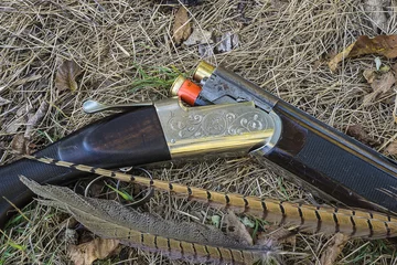 Zelfklevend Fotobehang Hunting gun, pheasant feathers on dry grass close up © stsvirkun